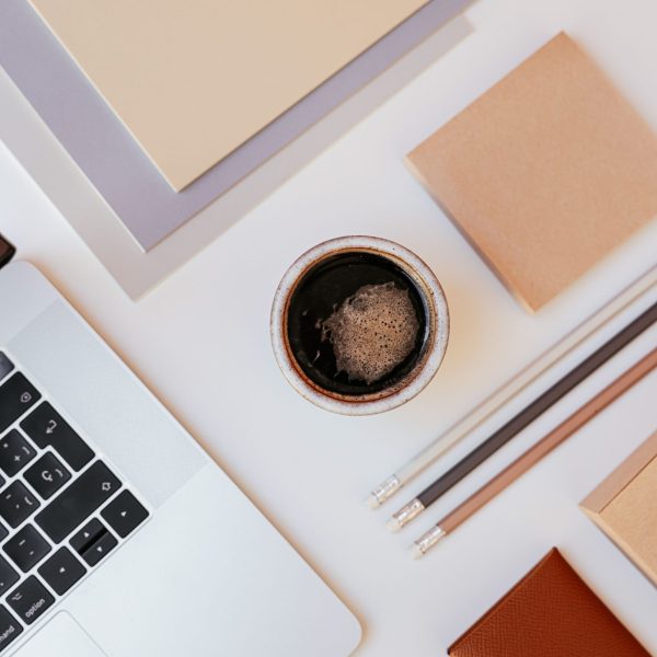 A top-down view of a minimalist desk setup featuring a laptop, coffee, and stationery items.